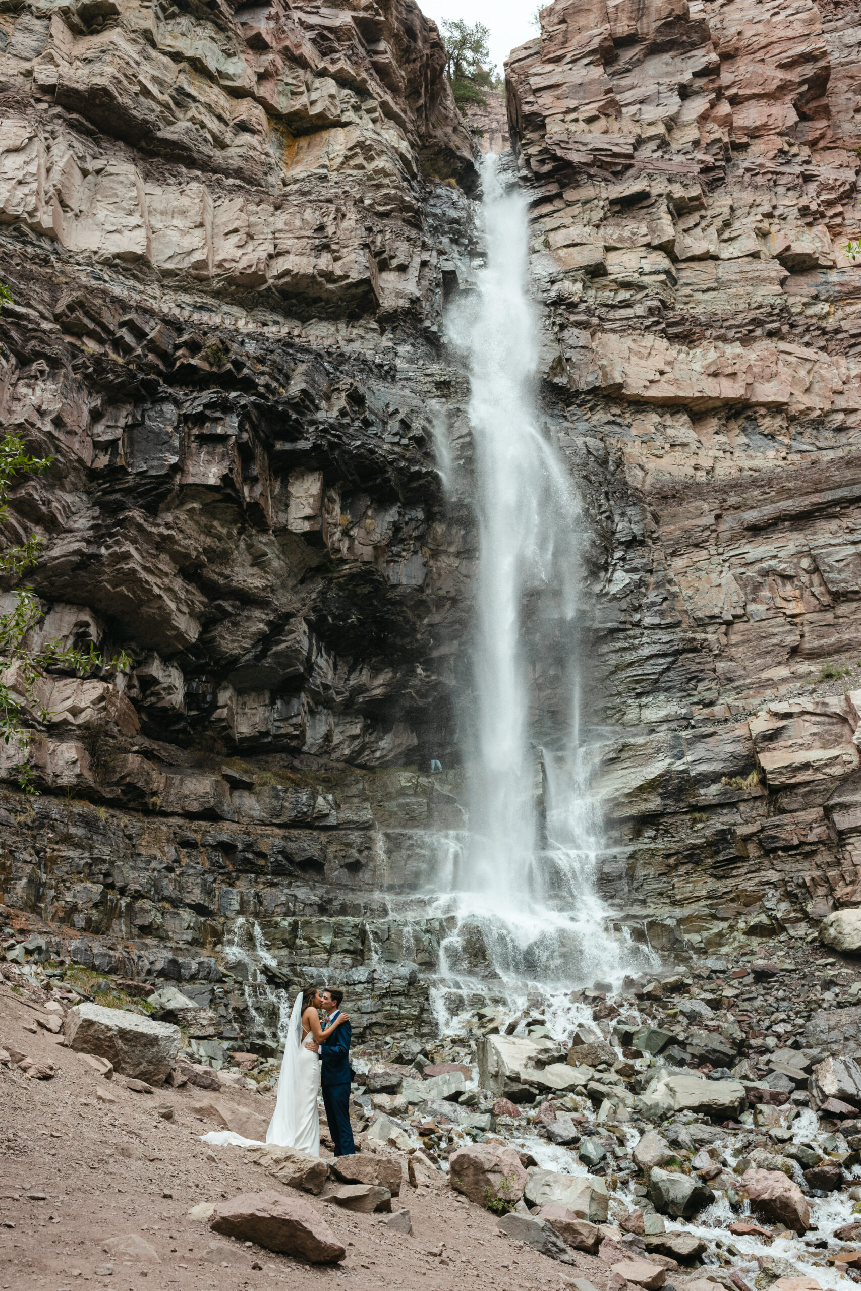 bride and groom standing under waterfall