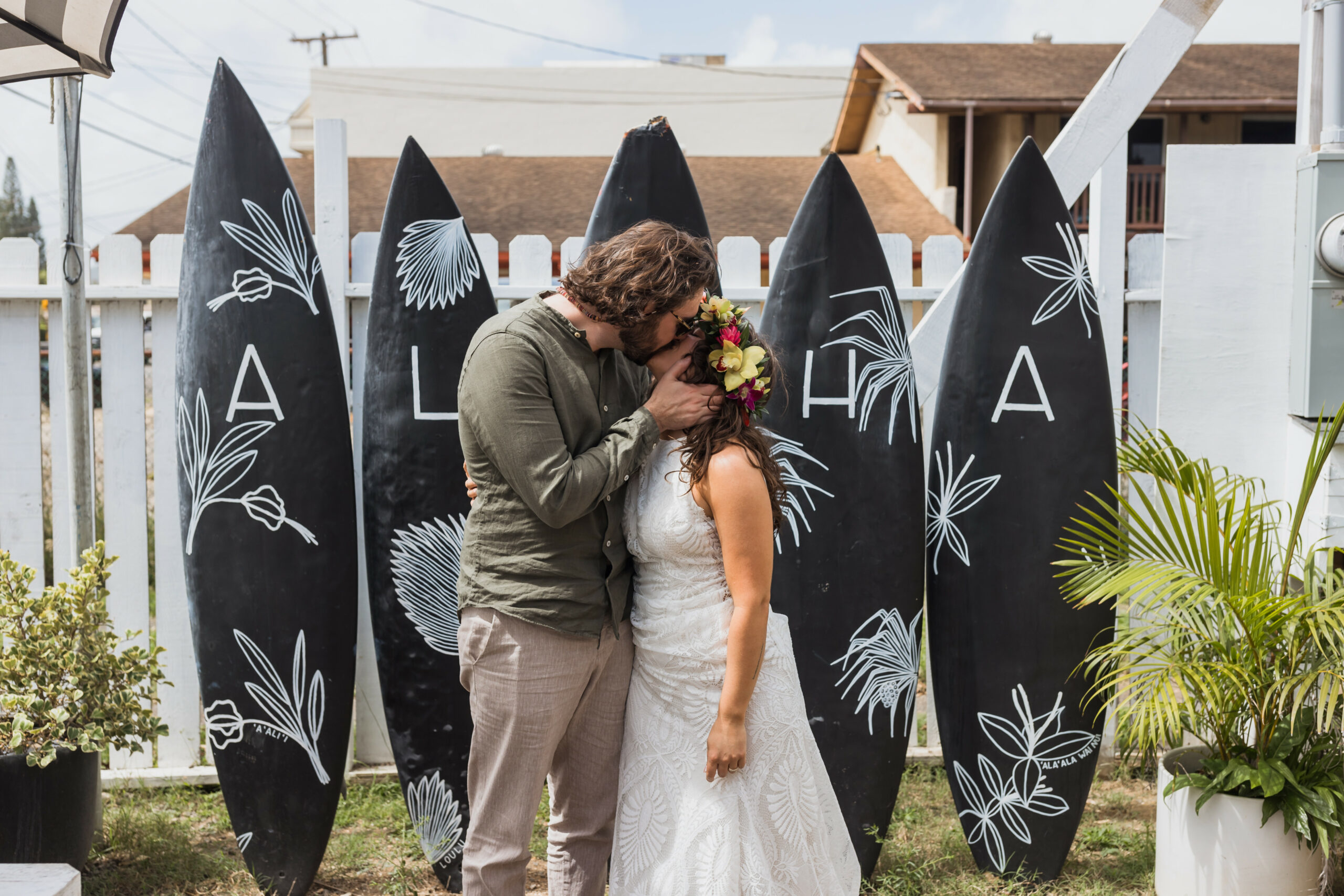bride and groom kissing in front of surfboards